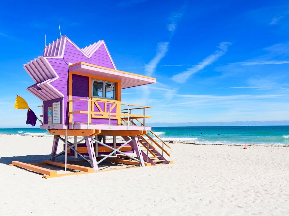 A colorful lifeguard tower on a sunny beach with clear skies and the ocean in the background.